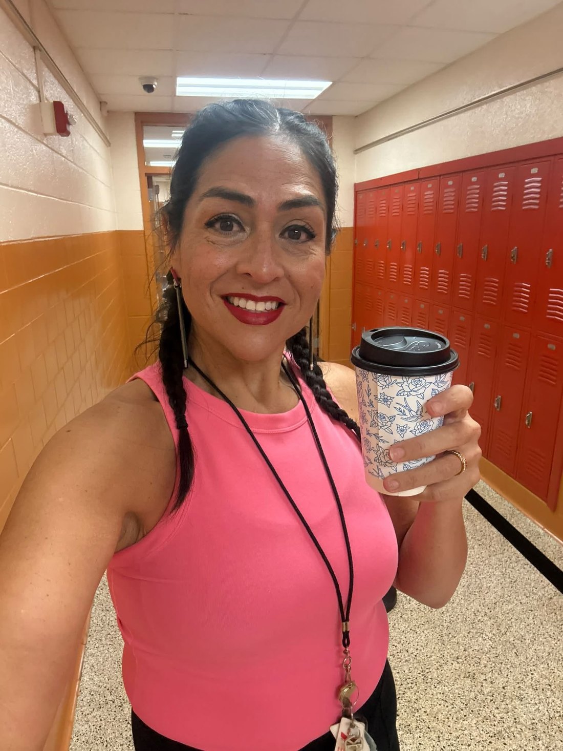 Yamile "Yaya" McBride in a school corridor, holding a coffee cup and smiling.