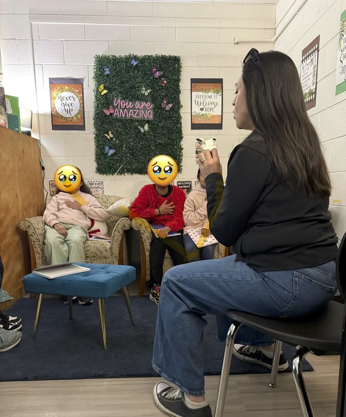 Yamile "Yaya" McBride leading a breathing exercise with students in a room decorated with "You Are Amazing" and "Everyone Is Welcome Here" signage.